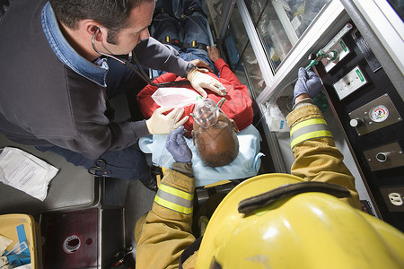男消防员和急救队医生在救护车中照顾一名受伤的老年男子背景
