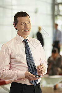中年商务人士与背景同事在办公室使用蓝牙 同时用手机做客的中年生意人;背景图片