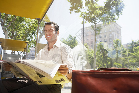 快乐的商务人士在公共汽车站看报纸时四处转眼背景