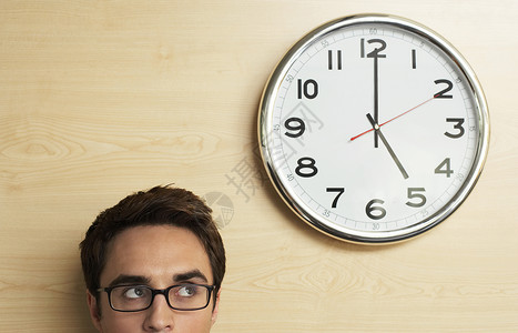年轻商务人士佩戴眼镜 在办公室的木墙上看钟表背景图片