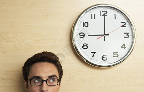 八点钟年轻商务人士戴眼镜看办公室木墙上时钟的头像背景