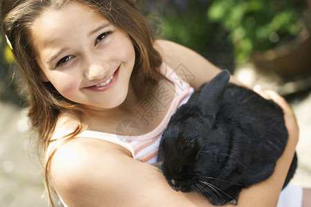一个快乐的年轻女孩的肖像 抱着兔子兔在后院背景图片