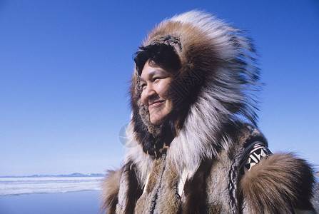 派克大衣穿着传统服装的爱斯基摩微笑女性在风中与清蓝天空对抗背景