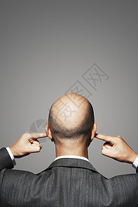 一个秃头商务人士的后视线 他用灰色背景来指着耳朵高清图片