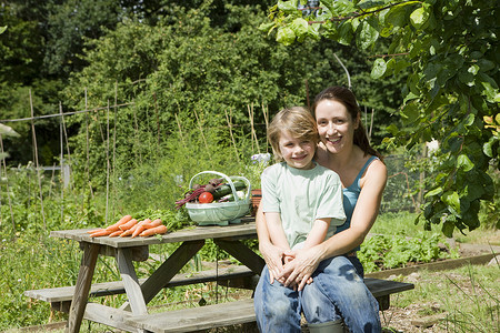 篮子和地段母亲和儿子一起坐在花园肖像中头发休闲微笑家长植物树木棕色服装个人桌子背景