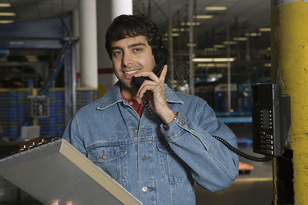 在工厂里使用电话微笑的年轻男子听力衣服技术工作服工人印刷拉丁水平生产幸福背景图片