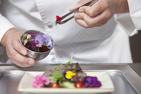 在商业性厨房的沙拉上搭配食用鲜花的男厨师中缝合背景图片