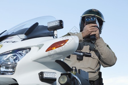 巡逻军官坐在摩托车上 通过超速计看车制服执法头盔物体衬衫交警法律车辆秩序绿色背景图片
