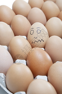 蛋包肠滑稽的面孔画在一个蛋上 被纸箱里的浅褐蛋包围着背景