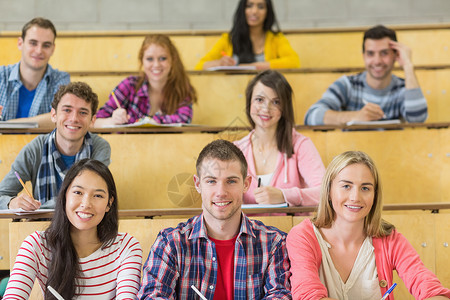 坐在礼堂的微笑的学生们笔记注意力大学女性研究所女士学生知识快乐混血背景图片