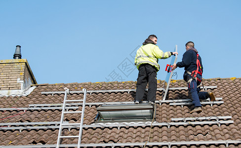 男人把太阳能电池板放在屋顶上学校工作网格工人安全帽建筑活力光伏梯子环境背景图片