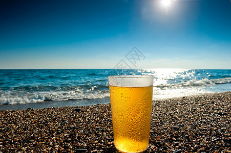 喝饮料的太阳冰啤酒杯 在海面背景上背景