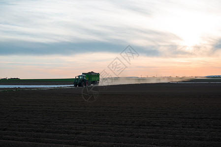 配备拖车的现代拖拉机农村机械收成农业农田灰尘天空土地牵引车日落背景图片