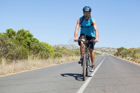 在开阔道路上骑自行车的运动员娱乐骑术男性活动农村蓝天头盔晴天阳光冒险背景图片