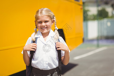 坐在校车旁边的可爱学生微笑着服务小学女孩小学生辫子知识金发女郎童年瞳孔快乐背景图片