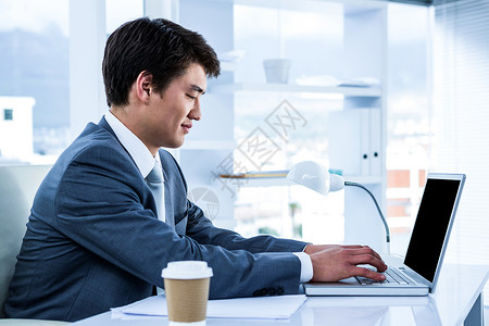 用心去弹钢琴使用电脑的亚洲生意人办公室男性专注桌子套装职业高脚杯老鼠屏幕职场背景