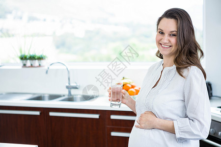 拿着一杯水的孕妇玻璃台面腹部微笑住所公寓桌子生长怀孕家居背景图片