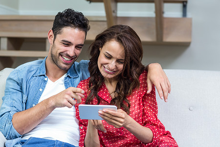 预兆使用智能手机微笑的情侣住所休闲沙发女士公寓夫妻幸福技术男性家庭生活背景