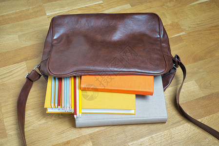 褐色书包皮革背包中的书本和铅笔手提包学生班级学习字帖褐色学校教育红色橙子背景