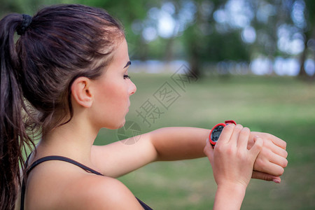 手腕上的手表女风情女孩在跑步时检查手腕上的监视跟踪器训练跑表车速女士手表运动女性背景