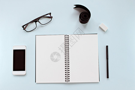 深红色螺旋彩带以空白笔记本 眼眼镜 智能电话 彩带和蓝背景办公文具为顶层工作空间台视图 创造性平板套装设计背景