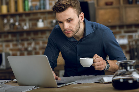 在家喝咖啡时使用笔记本电脑的青年男子厨房高清图片素材