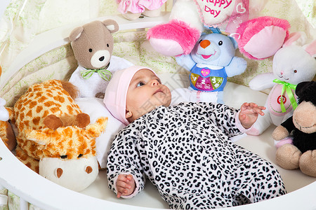 三年陈酿印章一个身着动物印章的女婴 周围围着填充动物印花睡衣玩具孩子柔软度快乐幸福婴儿床喜悦女孩背景