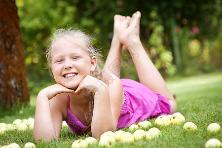 花园里可爱的年轻姑娘粉色小吃女孩草地果园裙子孩子水果孩子们绿色背景图片