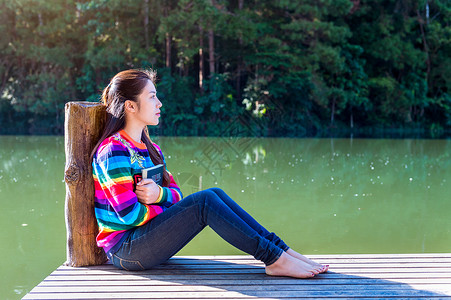 读码小女孩坐在码头上女士自由女性潮人头发支撑公园青少年码头太阳背景