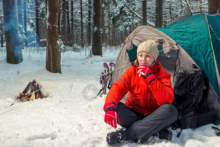 远征者活跃的疲累妇女坐在冬季森林帐篷附近背景
