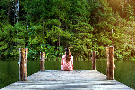 读码独自坐在湖边木桥上的女孩 泰国的潘阳背景