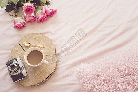 粉红色床单上躺在床上的咖啡旧老式相机 周围有玫瑰和笔记本 平躺风格的自由时尚家居女性气质工作区商业阴霾教育互联网旅行卧室闲暇生活背景图片