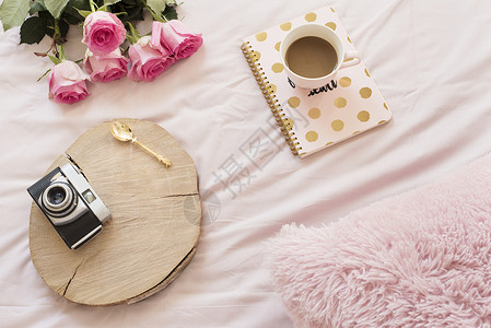 粉红色床单上躺在床上的咖啡旧老式相机 周围有玫瑰和笔记本 平躺风格的自由时尚家居女性气质工作区闲暇互联网博主阴霾卧室房间酒店生活背景图片