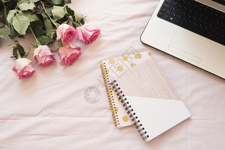 粉红色床单上的笔记本 膝上型电脑 一束玫瑰花 平躺风格的自由时尚家居女性气质工作区背景图片