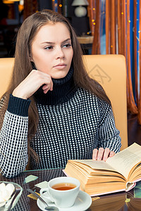 一个女孩带着一本书在咖啡厅的桌子上思考过 看着背景