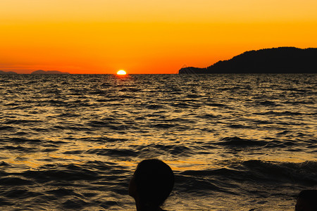 玩太阳的小孩躲在沙滩边 藏着橙色天空太阳波浪假期旅行日落支撑橙子地平线黄色海洋背景图片