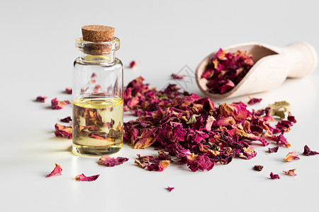 一瓶含干玫瑰花瓣的玫瑰必需油香味玻璃香气草本植物草药桌子治疗药品香精油按摩背景图片