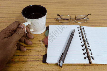 时光文案元素商务人士拿着一杯咖啡 带有眼镜和笔的商务口袋规划师准备好记录约会 商业静物概念与桌上的办公用品 准备好样机的空白页背景