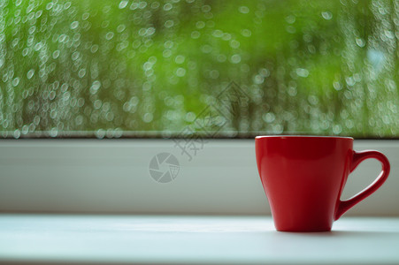 窗台边框白色窗台上的红咖啡杯 背景窗口和雨中 杯子位于边框右侧绿色咖啡红色太阳中心窗户背景