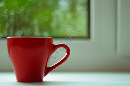 窗台边框白色窗台上的红咖啡杯 背景窗口和雨中 杯子位于边框左侧绿色太阳中心红色咖啡窗户背景