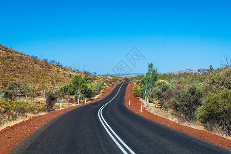 皮尔巴拉澳大利亚Karijini国家公园山丘之间有深薄油塔的黑暗公路背景