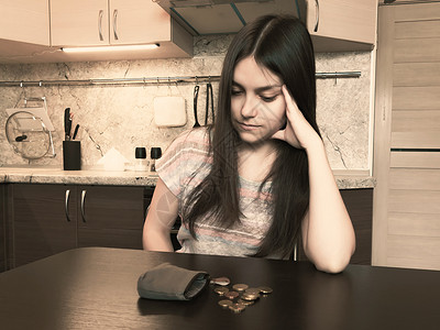 财政问题概念 一名长头发黑发的年轻失望妇女坐在一个旧空钱包旁边 桌上有数枚硬币 注失败信用货币情绪厨房烦恼商业债务女性女士女孩高清图片素材