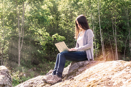 博客顶部素材年轻美丽的女孩坐在森林的一块大石头上 正在用笔记本电脑工作 自由主义概念日落自由职业者互联网女士网上购物商业季节矿业远足教育背景