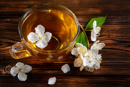 茉香奶茶菲利亚德尔弗斯的花朵 在叫茉莉或假橙和杯子的地方 黑木桌上有香茉菊茶绿茶梅花饮料茶点植物玻璃桌子芳香香气照片背景
