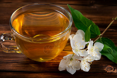 茉莉花香菲利亚德尔弗斯的花朵 在叫茉莉或假橙和杯子的地方 黑木桌上有香茉菊茶疗法玻璃茶碗植物茶点绿茶早餐香气芳香照片背景