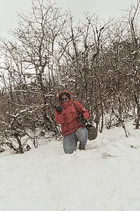 我有一个雪鞋一个穿着红色套头夹克的女人微笑着快乐地享受着第一场雪的玩耍和向空中扔雪球的肖像 在冬天享受下雪天的景色 农村查谟和克什米尔暴背景