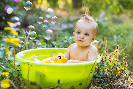 绿色与黄色泡泡盆子里的托德勒男孩 用泡泡和鸭玩具洗澡喜悦身体太阳婴儿享受绿色孩子黄色小鸭子橡皮背景