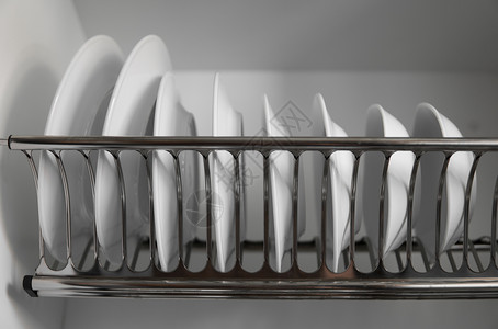 许多对象带有大而漂亮的白色干净盘子的洗碗机金属架 传统舒适的厨房 打开白色盘子排水壁橱 里面有玻璃和陶瓷湿盘子 盘子 碗 在架子上晾干餐背景