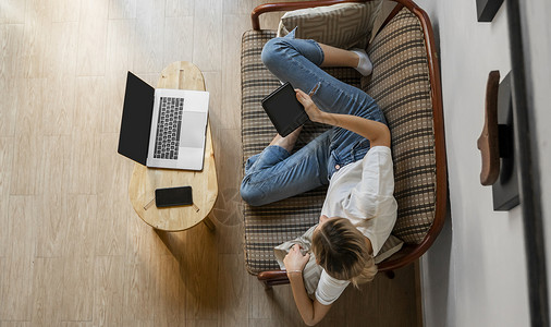 综艺花字AE女人躺在沙发上 一边使用笔记本电脑一边休息 一边使用 ae 阅读器 在线学习和工作 自由职业者 女孩正在用她放在沙发上的笔记本工背景