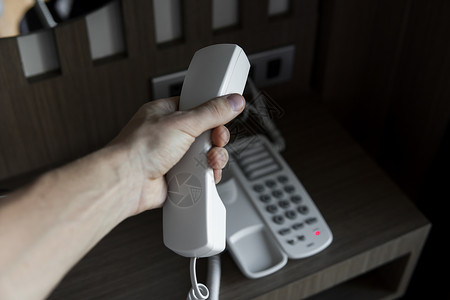 男人手握着白色古老电话的听筒 在旅馆的棕色桌子上有灰色棍棒塑料绳索咨询旋转模拟中心商业热线服务乡愁背景